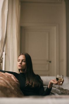 a woman sitting on a couch with a glass of wine in her hand and looking off into the distance