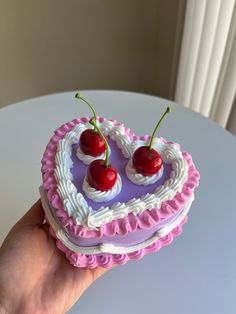 a heart shaped cake with two cherries on top is being held by a hand