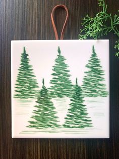 a ceramic ornament with green trees painted on it and a brown leather cord