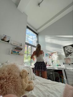 a woman standing on top of a bed next to a teddy bear in front of a window