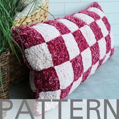 a red and white checkered pillow sitting next to a basket with grass in it