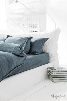 a bed with blue linens and pillows on top of it next to a stack of magazines