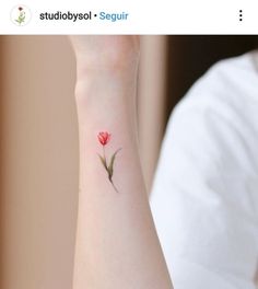 a woman's wrist with a small red flower on the left side of her arm