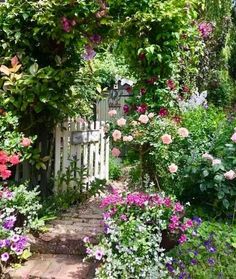 a garden filled with lots of flowers next to a white gate covered in greenery