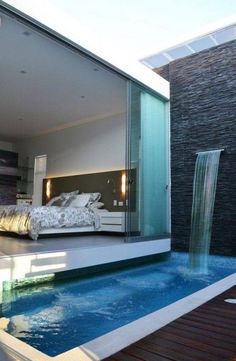 a bed sitting next to a swimming pool near a building with a waterfall in it