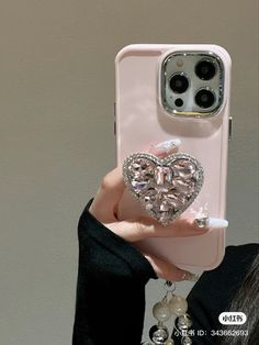 a woman holding up a pink phone case with a heart shaped diamond in the middle