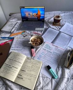 an open laptop computer sitting on top of a bed next to books and other items