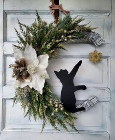 a black cat sitting on top of a wreath next to a white door with snowflakes and pine cones