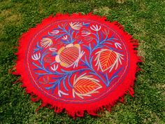 a red and blue round rug with leaves on it sitting in the middle of grass