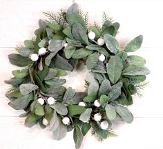 a wreath with green leaves and white flowers on a wooden surface, hanging from the wall