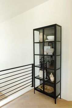 a black bookcase sitting on top of a wooden floor next to a metal railing