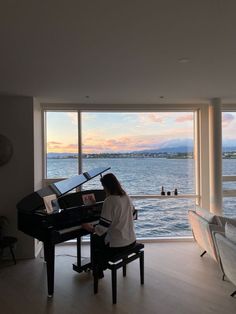 a woman sitting at a piano in front of a large window overlooking the water and buildings