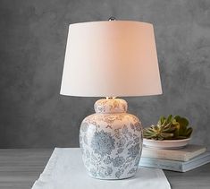 a white and blue vase sitting on top of a table next to a lamp