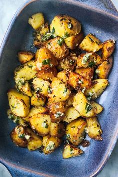 roasted potatoes with herbs in a blue bowl on a marble countertop, ready to be eaten