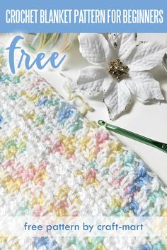 a crocheted blanket next to some yarn and a white flower on a table