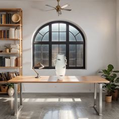 a table with a vase on it in front of a window and bookshelves