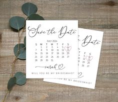 two save the date cards on top of a wooden table with eucalyptus leaves and greenery