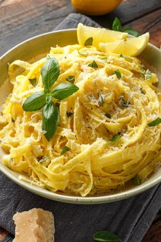 a bowl filled with pasta and garnished with fresh basil on the side next to lemon wedges