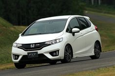 a white honda fit driving down a road