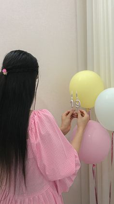 a woman is holding balloons in front of her face and looking at the wall behind her