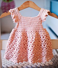 a pink crocheted dress hanging on a wooden hanger in front of a bed