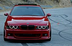 the front end of a red car parked in a parking lot next to a hill