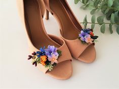 a pair of women's shoes with flower decorations on them sitting next to a plant