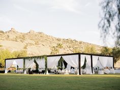 an outdoor wedding venue with white drapes and tables set up in front of the mountains