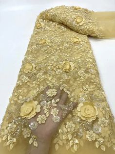 a person is touching the fabric with their hand on it's side, which has yellow flowers and gold sequins all over it