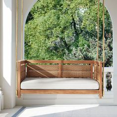 a wooden swing bed hanging from a ceiling in front of a window with trees outside