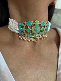 Handcrafted by fine jewelry artisans, this stunning choker necklace set is the perfect accessory for destination weddings and special occasions. Made of 925 silver, the choker features striking turquoise stones and delicate freshwater pearls, adorned with elegant golden ball hangings that add a touch of luxury. This timeless piece is designed to make you stand out. Necklace Weight: 56 grams Materials: 925 Silver, Turquoise, Freshwater Pearls, Golden Ball Hangings Closure Type: Hook closure and is adjustable. The set includes beautifully matching earrings that complete the look. Earrings Weight: 12 grams per pair. Earrings Dimensions: Length is 2 cm and width is 2 cm. Closure Type: Push Back Closure Add this one-of-a-kind, radiant choker set to your collection and let its unique design make Handmade Elegant Turquoise Choker, Elegant Handmade Turquoise Choker, Turquoise Beaded Fusion Jewelry, Turquoise Fusion Jewelry For Wedding, Elegant Turquoise Jewelry For Celebration, Traditional Turquoise Choker Jewelry, Traditional Turquoise Choker Necklace, Festive Turquoise Beaded Jewelry, Turquoise Beaded Jewelry For Celebration