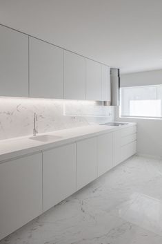 an empty kitchen with white cabinets and marble counter tops, along with a window that looks out onto the street