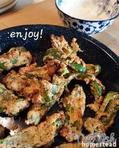 fried vegetables on a black plate with the words enjoy written above them and a bowl of yogurt in the background