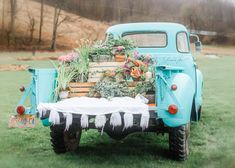 an old blue truck with flowers and plants in the back