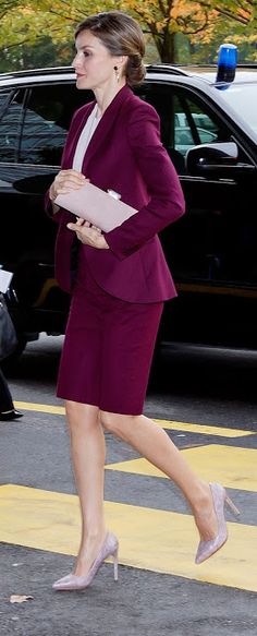 a woman in a purple suit and heels walking across the street with her hand on her hip