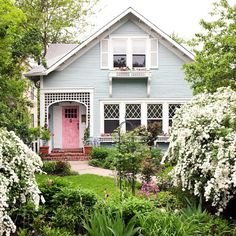 a blue house with pink door surrounded by greenery and flowers on the front lawn