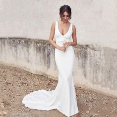 a woman in a white dress is standing by a wall and posing for the camera