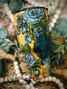 a yellow and blue flowered cup sitting on top of a table next to green leaves