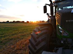 a tractor is parked in the middle of a grassy field at sunset or dawn with the sun shining behind it