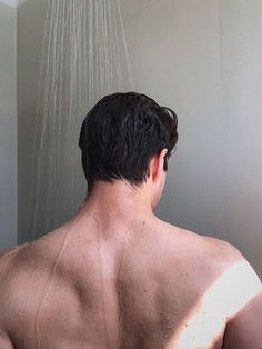 a man is standing in the shower with his back turned to the camera and it's raining