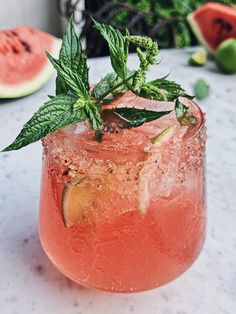 a close up of a drink on a table with watermelon slices and mint