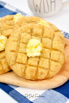 two cookies with butter on top sitting on a wooden plate next to a cup of coffee