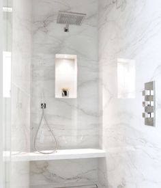 a bathroom with white marble walls and flooring, including a shower head in the corner