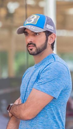 a man in a blue shirt and hat with his arms crossed looking off to the side