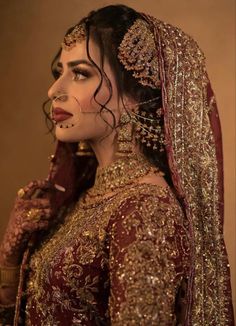 a woman in a red and gold bridal outfit with jewelry on her head, looking off to the side