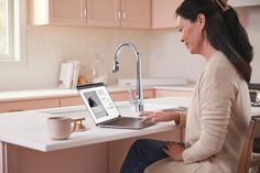 a woman sitting at a kitchen counter using a laptop computer