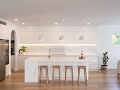 an open kitchen with white cabinets and counter tops, along with bar stools in front of the island