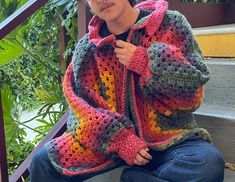 a woman sitting on the steps wearing a crocheted jacket and jeans with her hands in her pockets