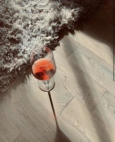 a glass of red wine sitting on top of a wooden floor next to a rug