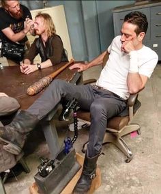 a group of men sitting around a wooden table in an office setting with one man talking on the phone